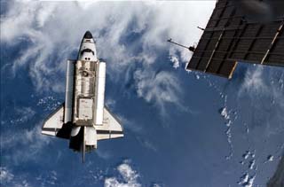 View of the departing space shuttle Atlantis as seen from the Mir space station. A cloudy Earth forms the background. 